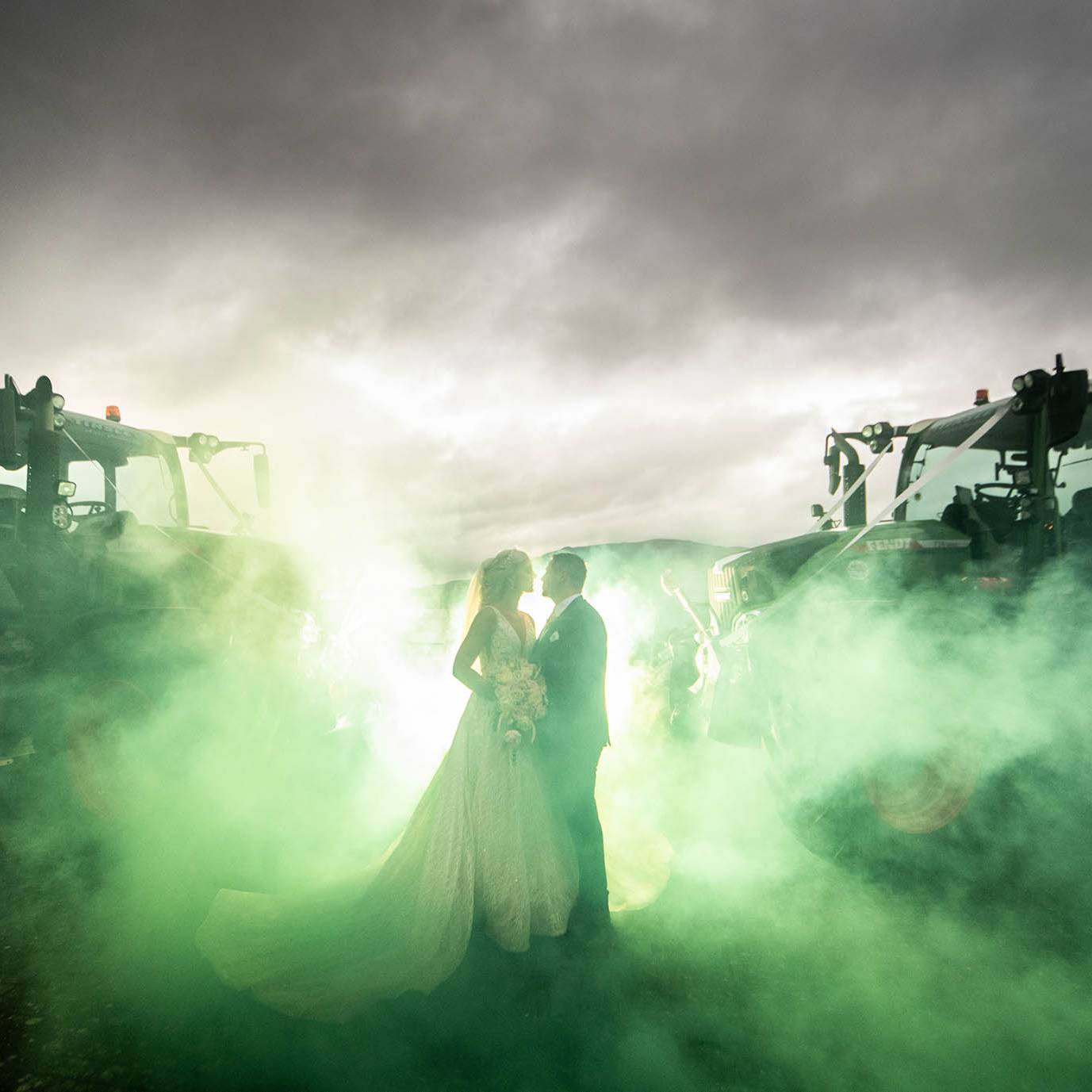 Tips for choosing your wedding photographer - Bride & Groom kissing in between 2 Fendt Tractors - Green smoke bombs create a dramatic backdrop
