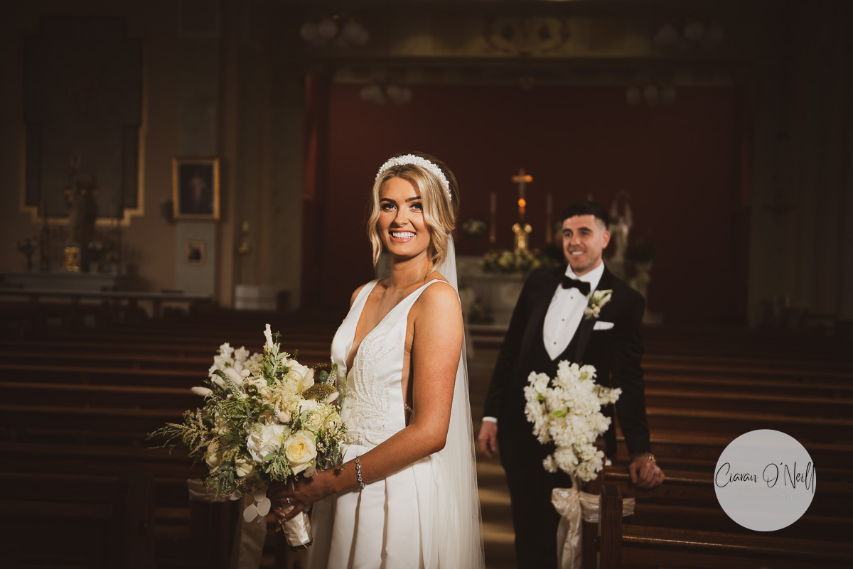 Bride standing in the aisle as the groom looks on lovingly behind her