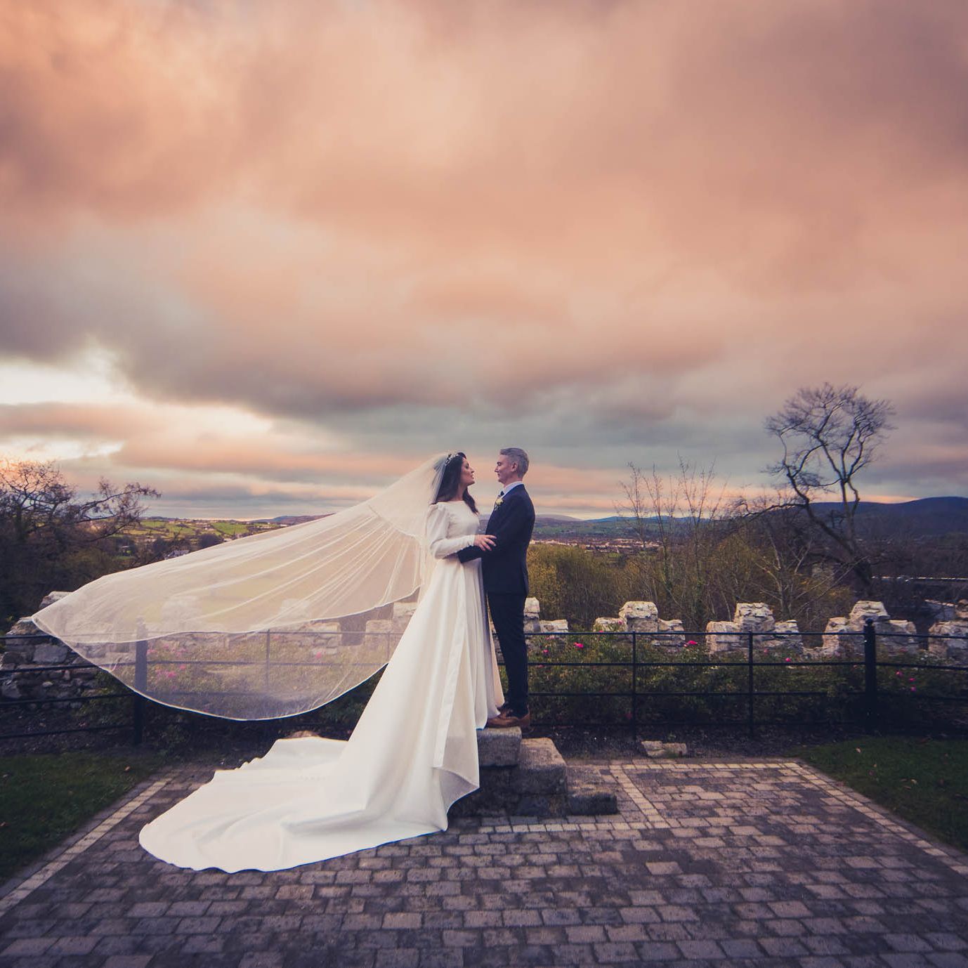 Birde and groom standing outside Killeavy Castle with her veil flowing in the wind