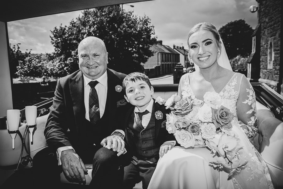 The bride, her son and her father sit in the car posing for a photo