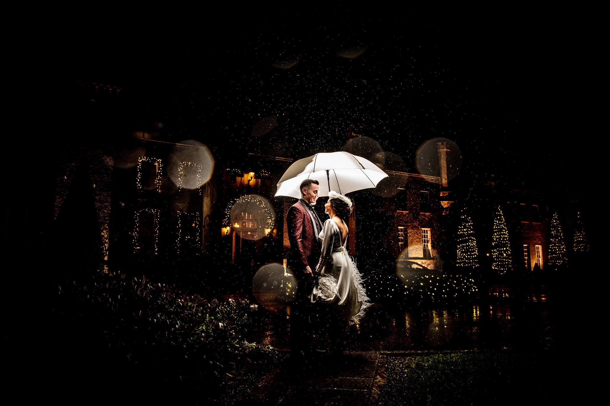 Bride & Groom standing under an umbrella - embracing the rain - outside Castle Bellingham