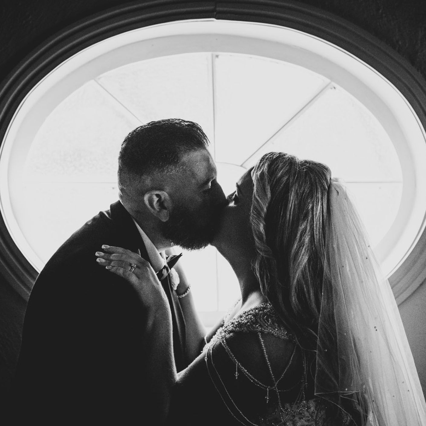 Couple kissing, silhouetted by the beautiful window in the background