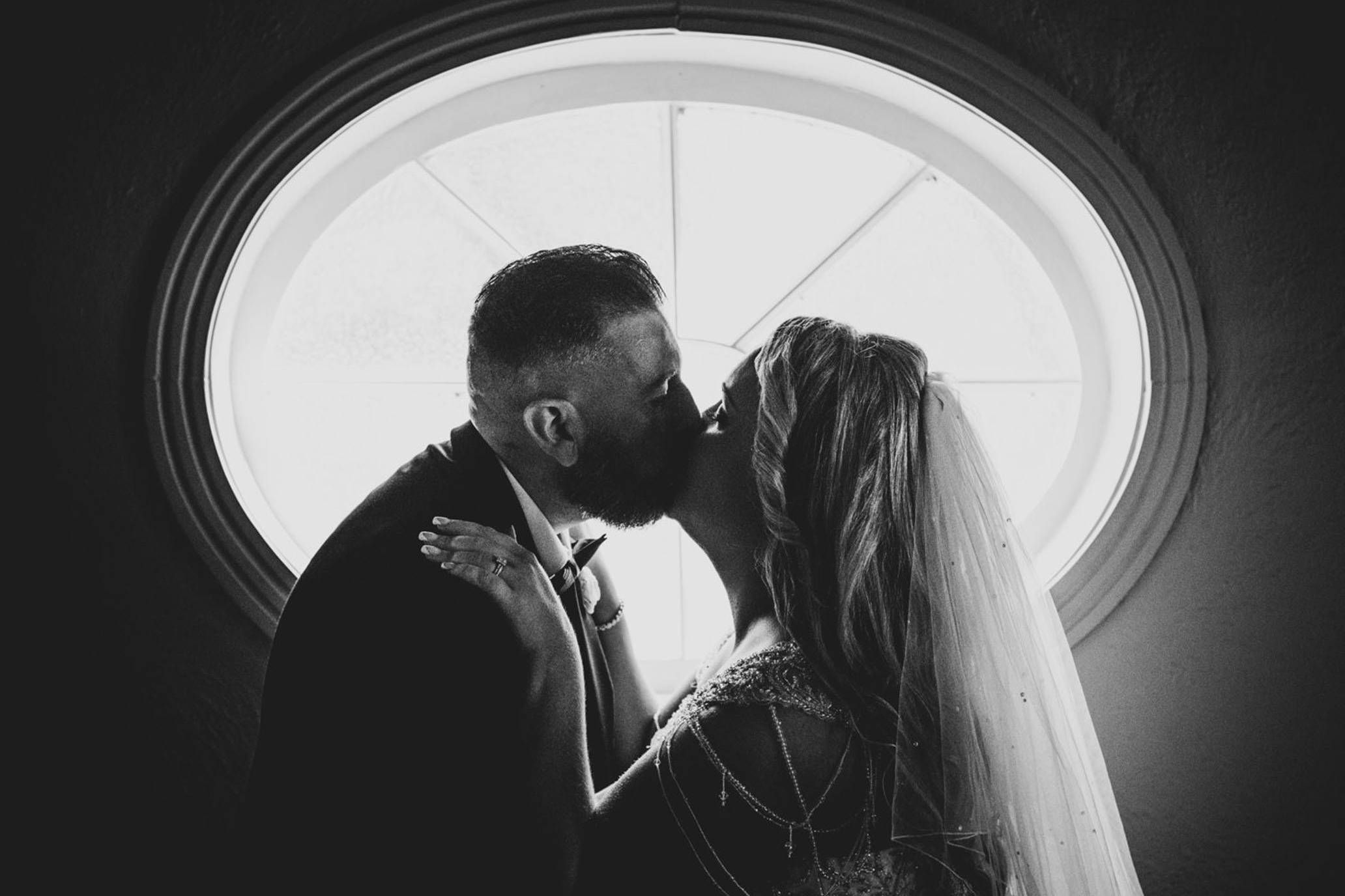 Couple kissing, silhouetted by the beautiful window in the background