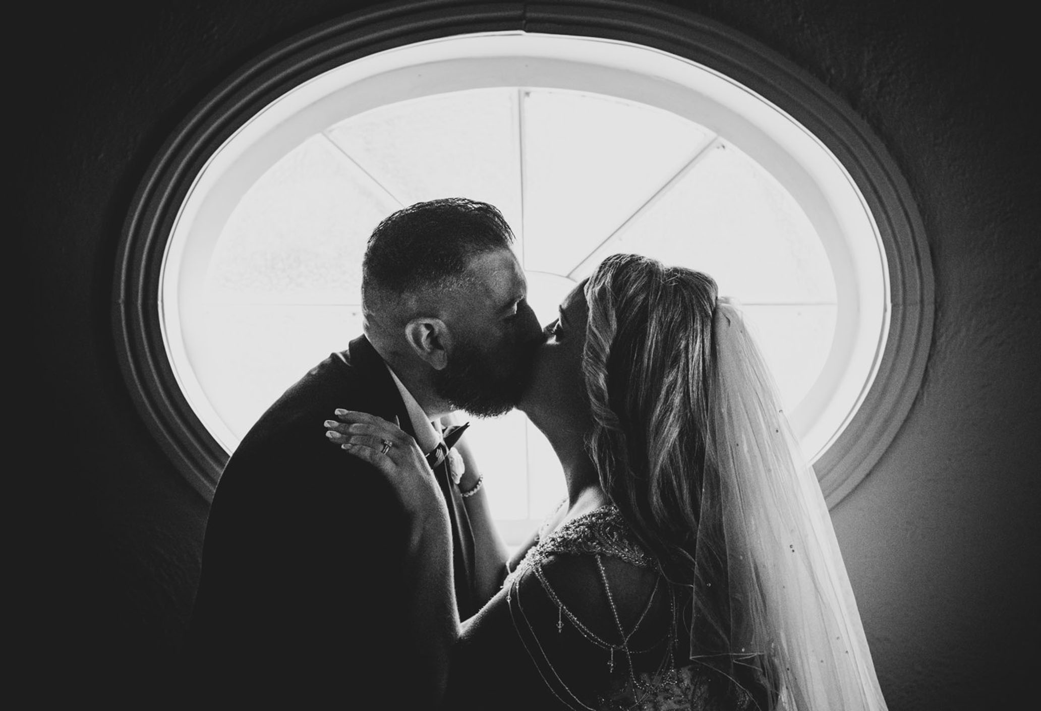 Couple kissing, silhouetted by the beautiful window in the background