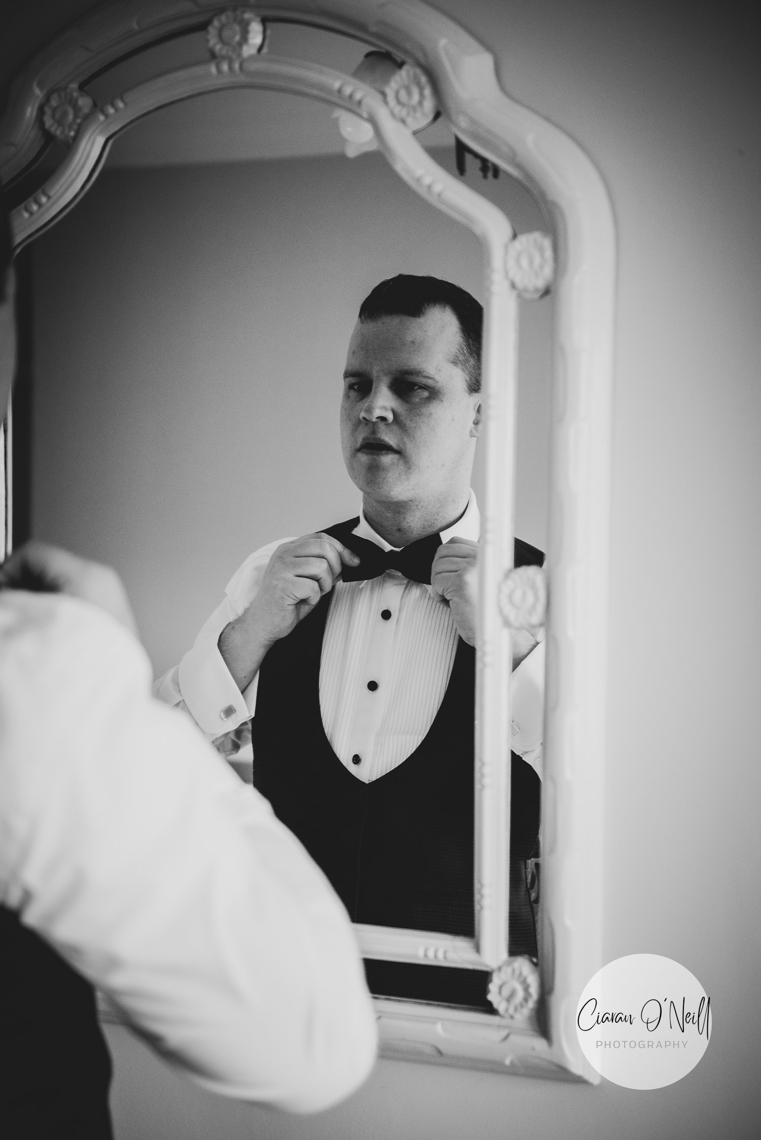 Groom tying his bow tie in the mirror