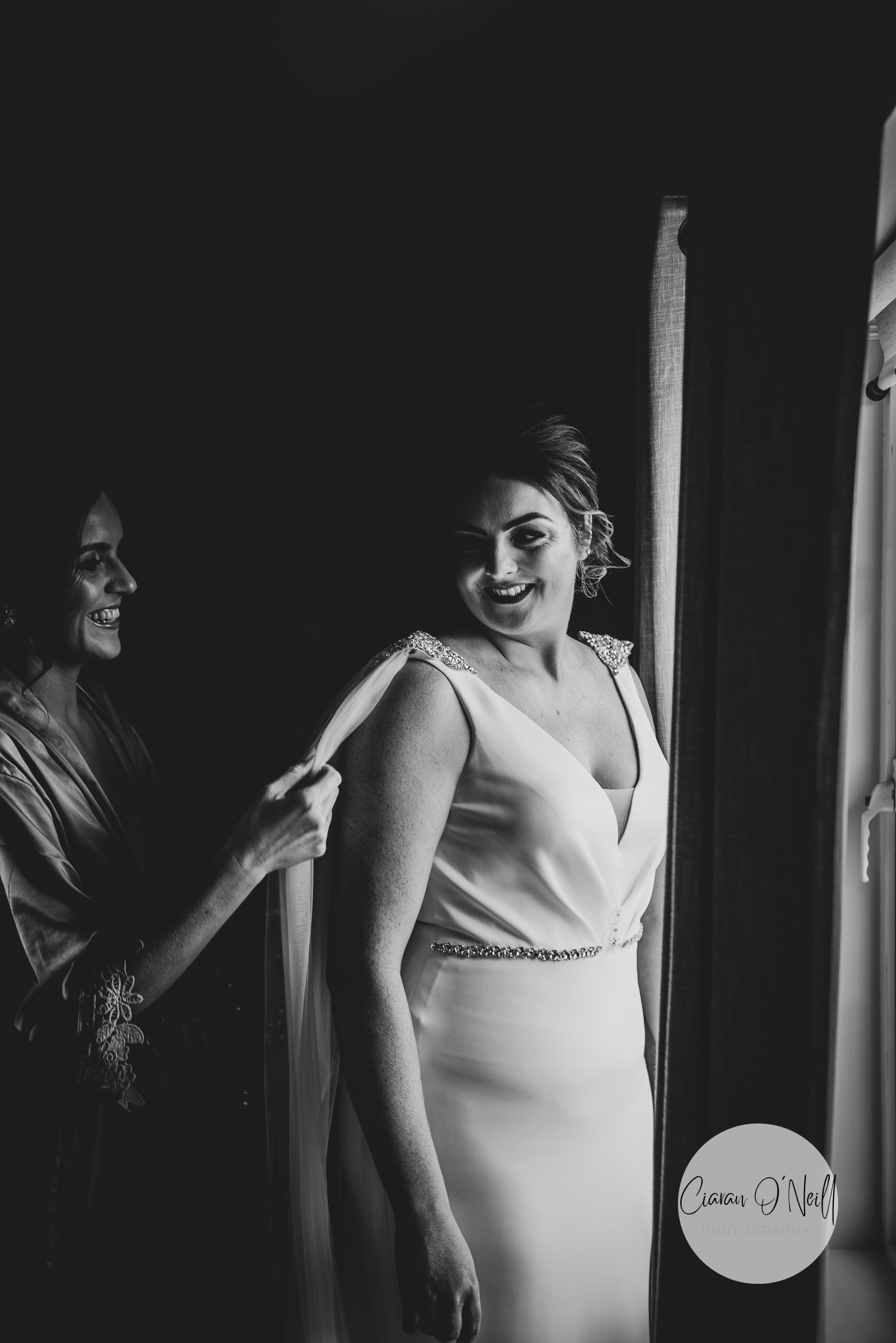 Bridesmaid helping the bride get ready beside a large window