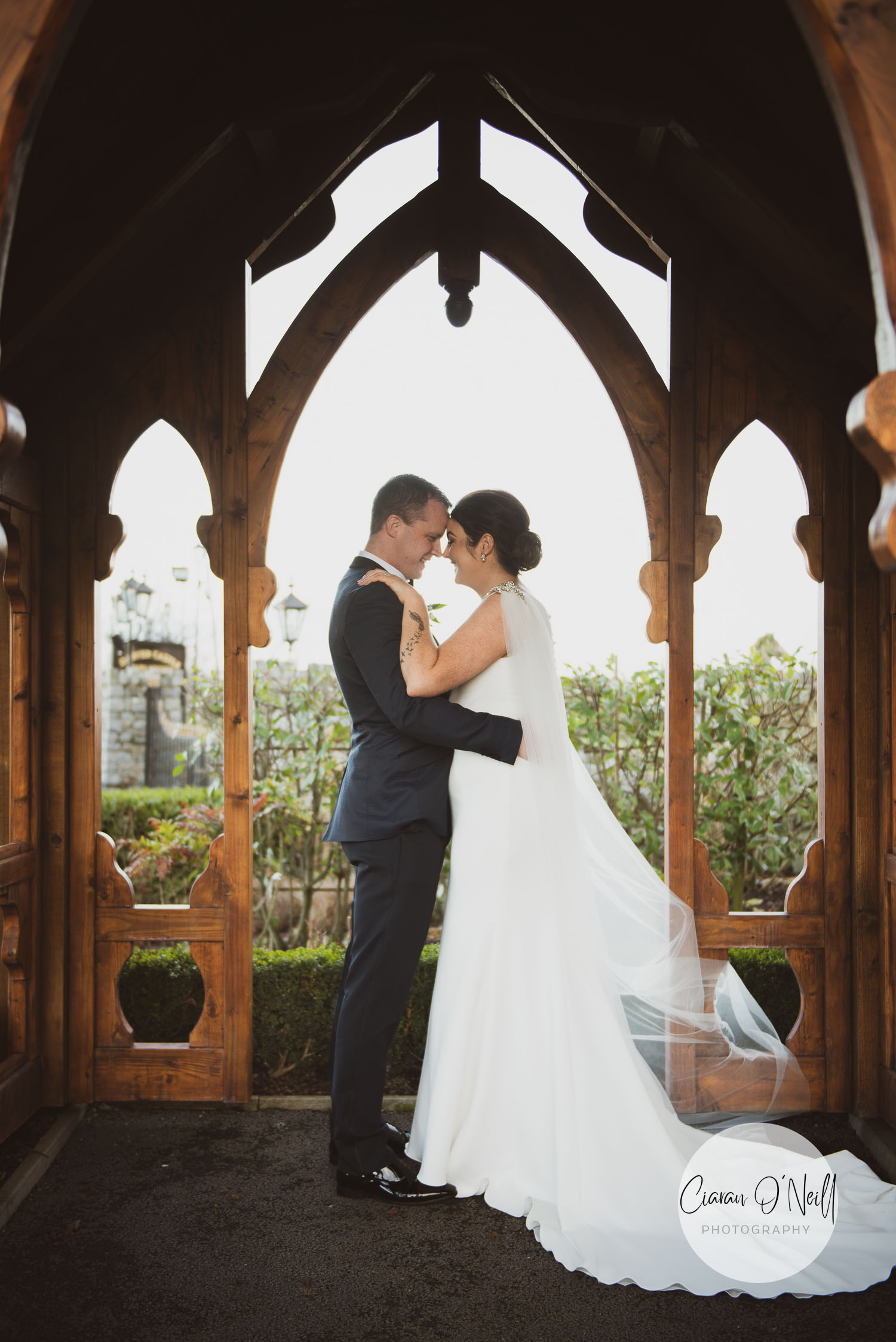 bride and groom standing in a wooden church style archway in a garden
