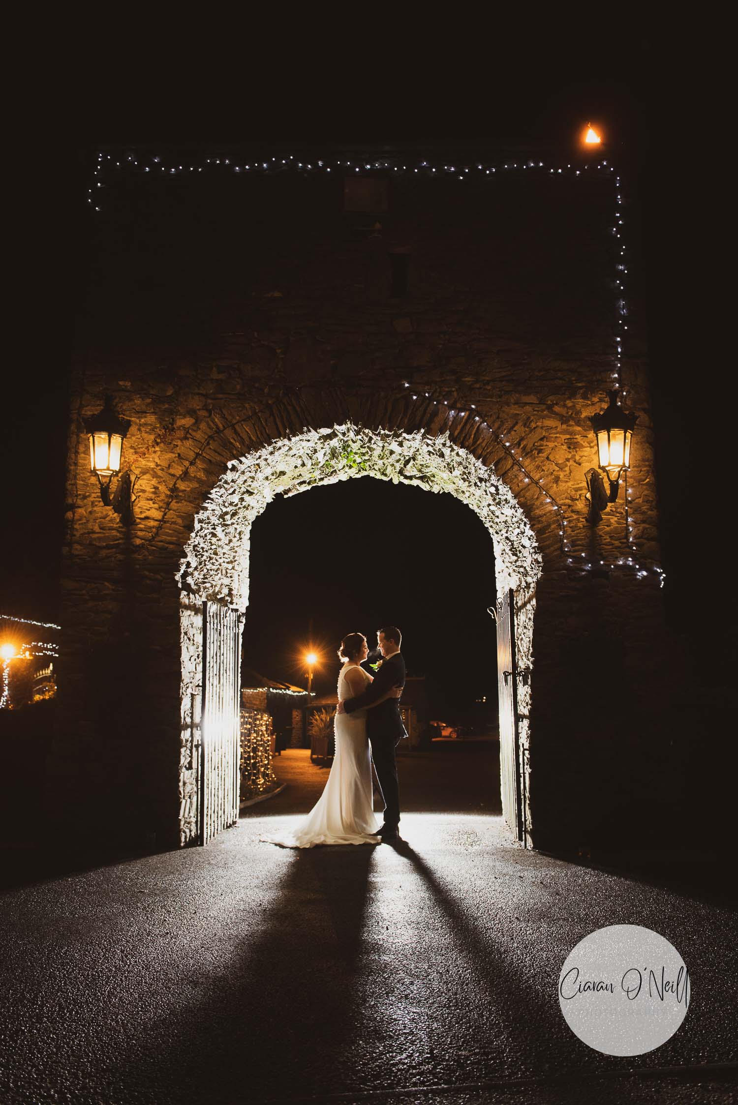 Bride and groom under an arch after dark lit from behind