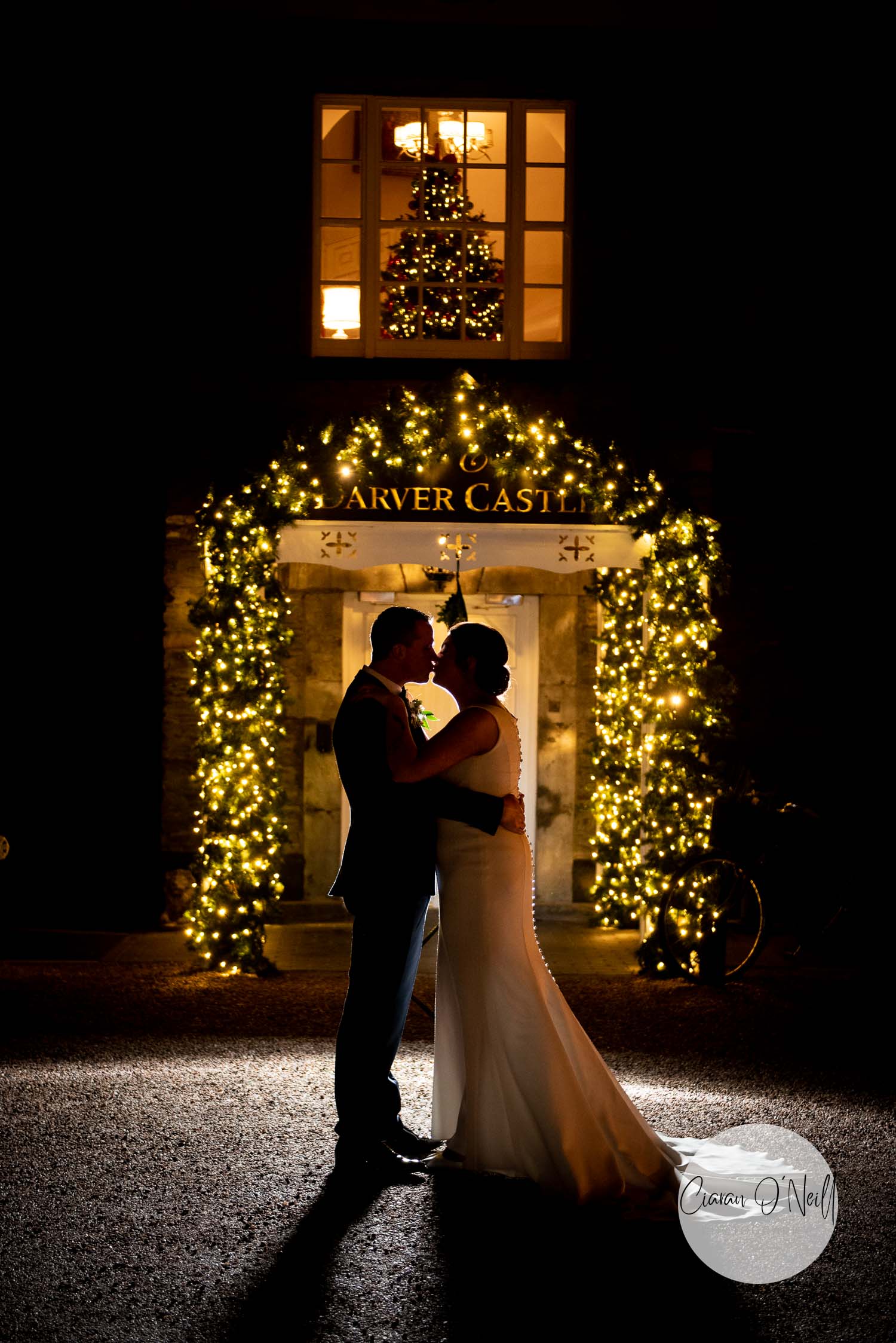 silhouette of bride and groom in front of a floral arch lit with fairy light outside an irish castle