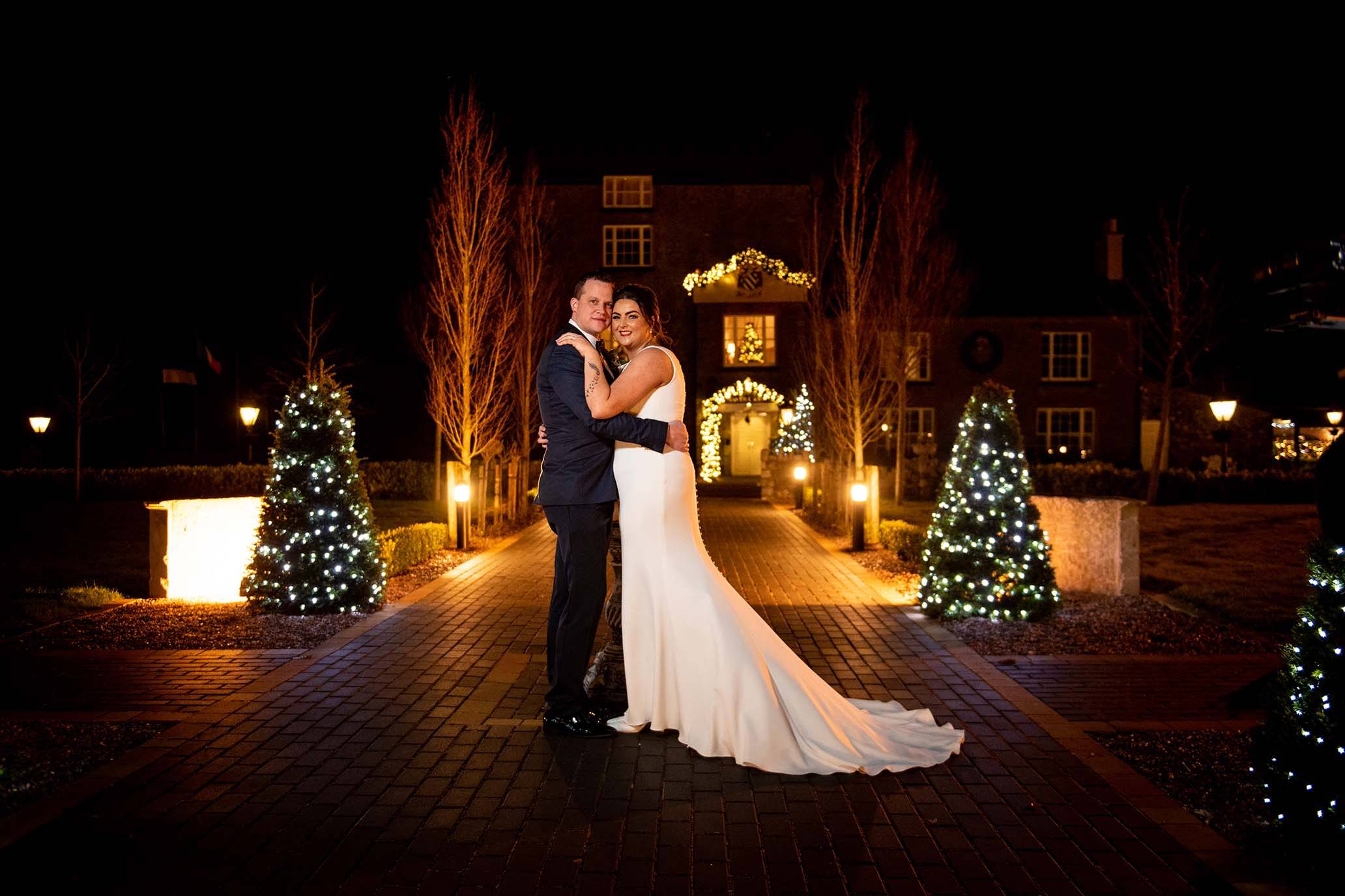 Bride and groom embracing after dark out side Darver castle with chridtmas lights in background