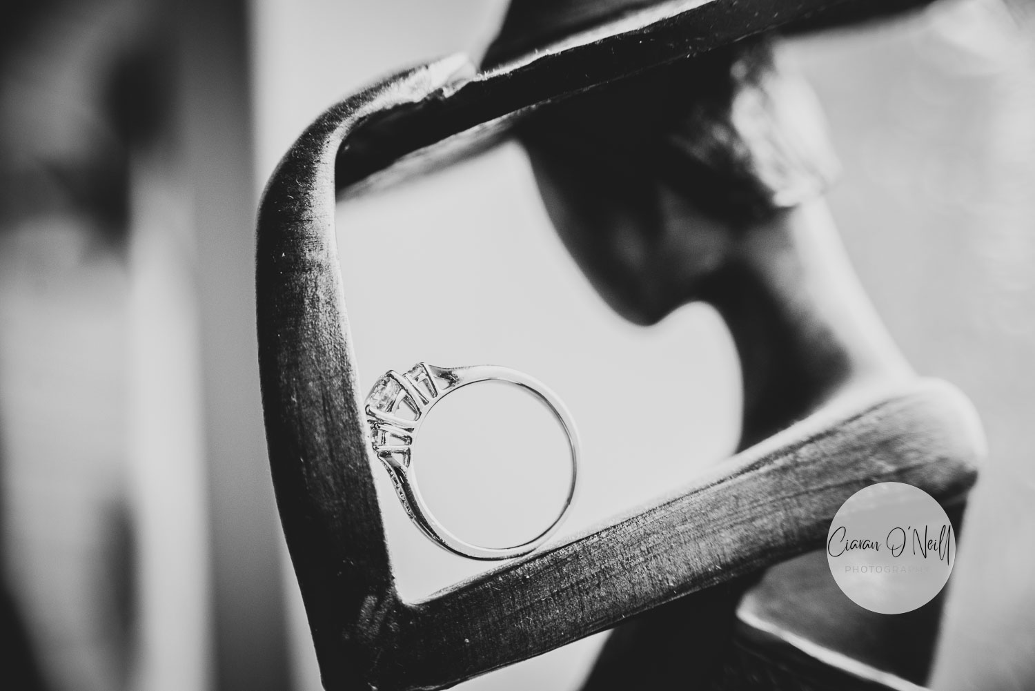 Black and white photo of diamond engagement ring positioned on top of wooden figure