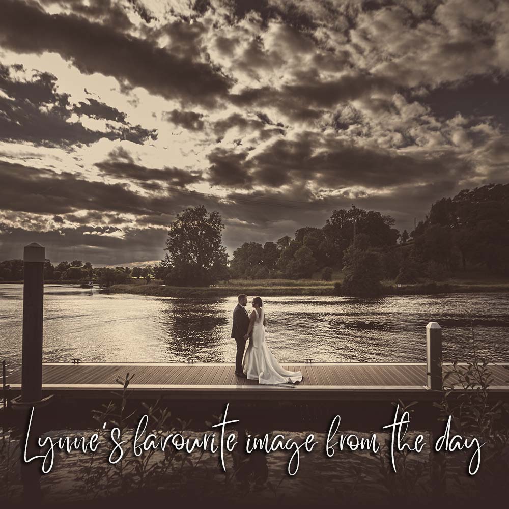 Romantic sepia coloured photo of bride and groom standing on a pier at sunset in Lough Erne
