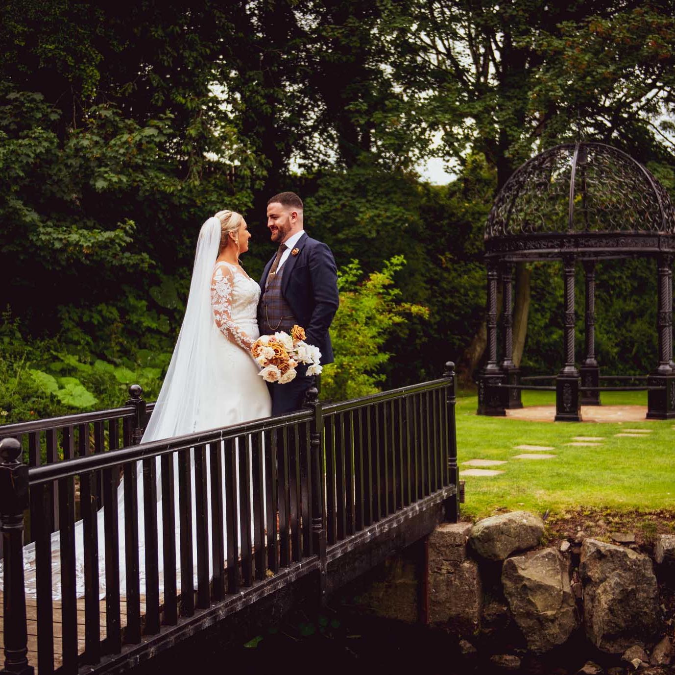Melissa & Aidan - standing on a bridge looking lovingly at each other at Ballygally Castle