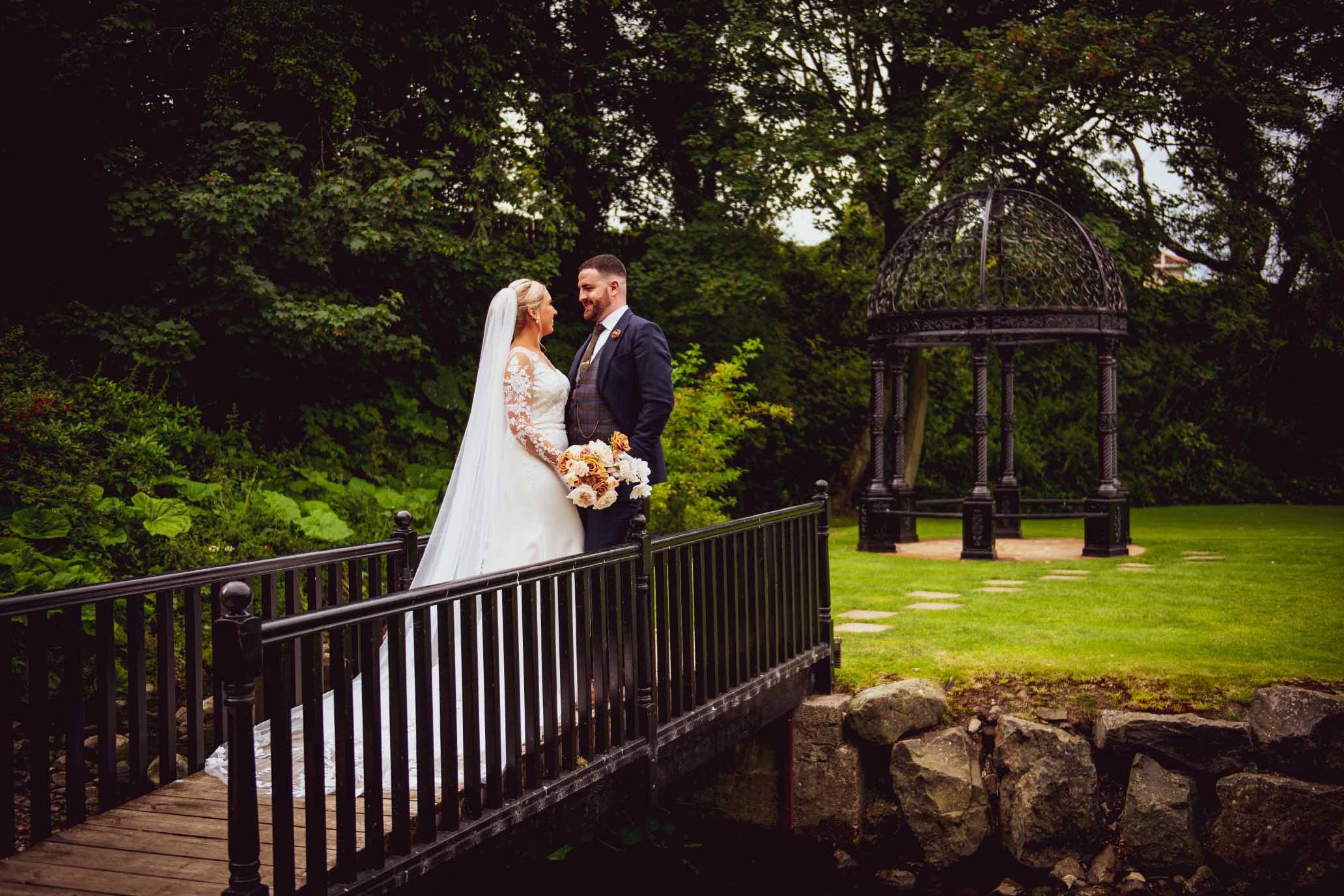 Melissa & Aidan - standing on a bridge looking lovingly at each other at Ballygally Castle