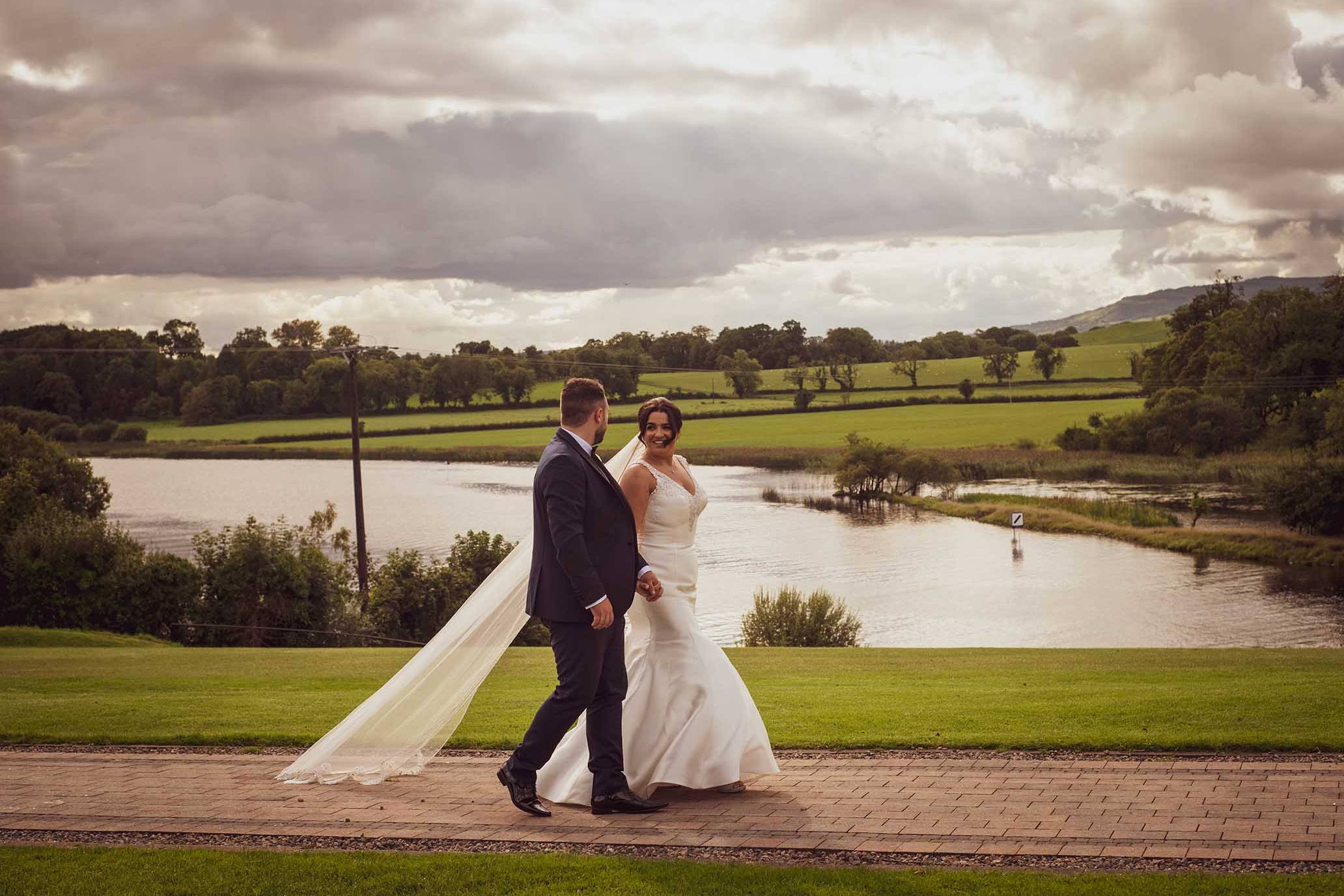 Romantic bride and groom walking past lake at Killyhevlin hotel Fermanagh