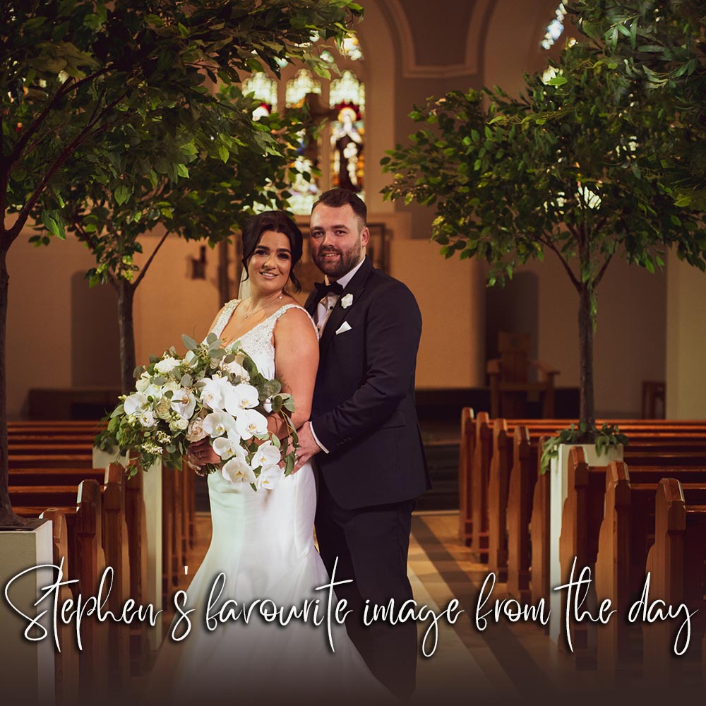 Groom embracing bride from behind in the aisle of the church with decorative trees behind
