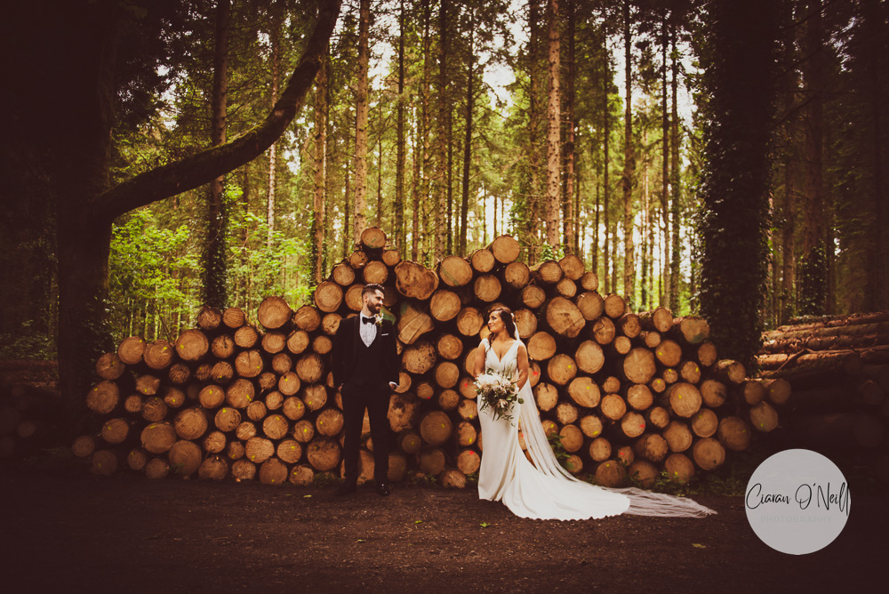 Bride & Groom looking at other in front of a pile of logs in Old Castle Archdale