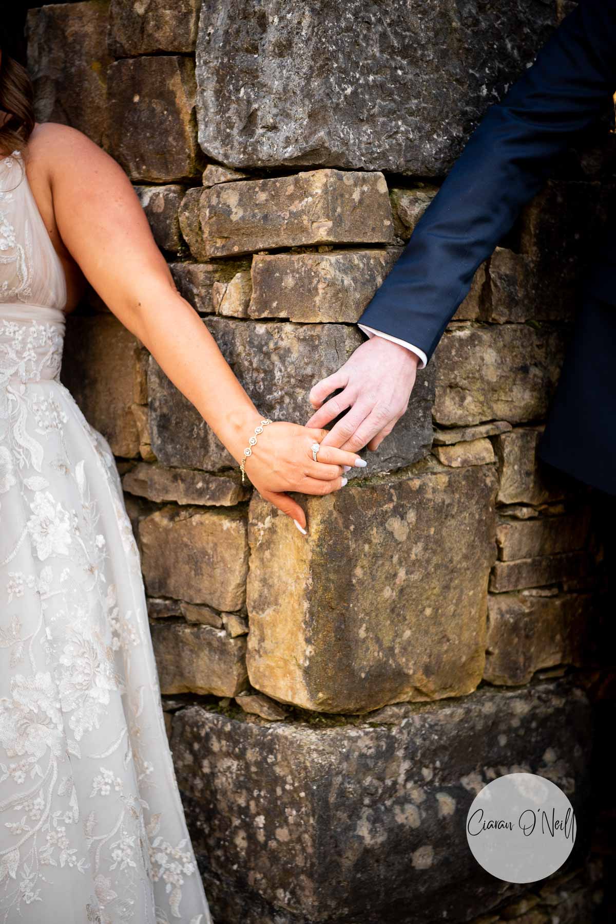 Bride and groom touching hands around a corner in the wall