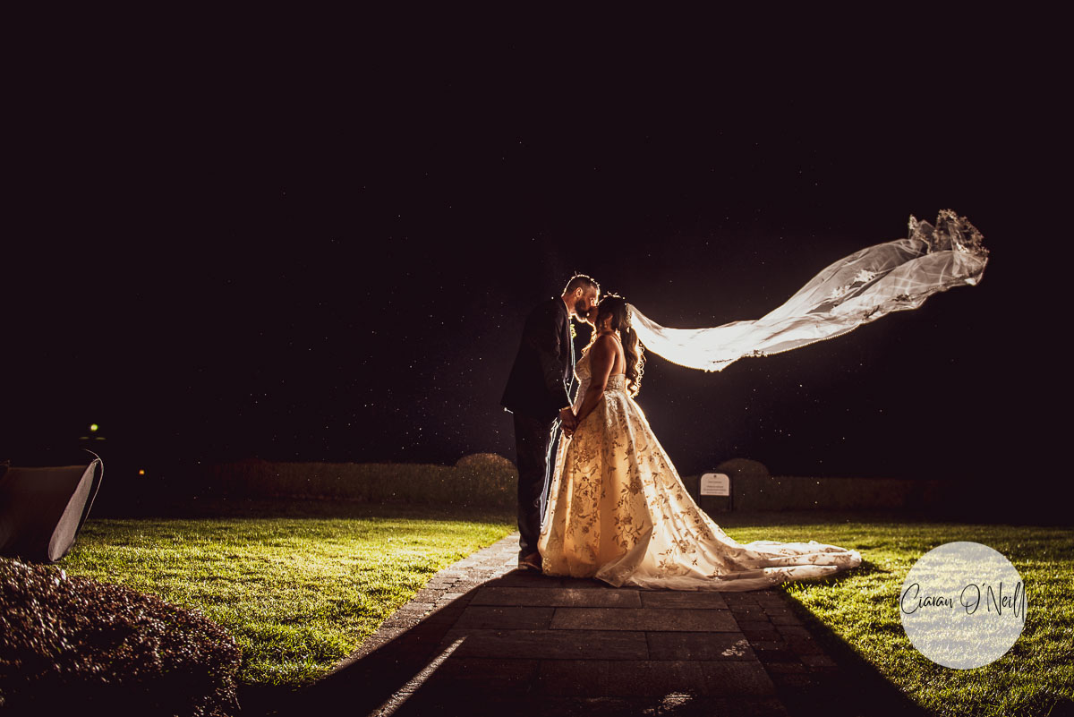 Dramatic photo of the veil flowing in the wind. Shot at night -the couple are kissing