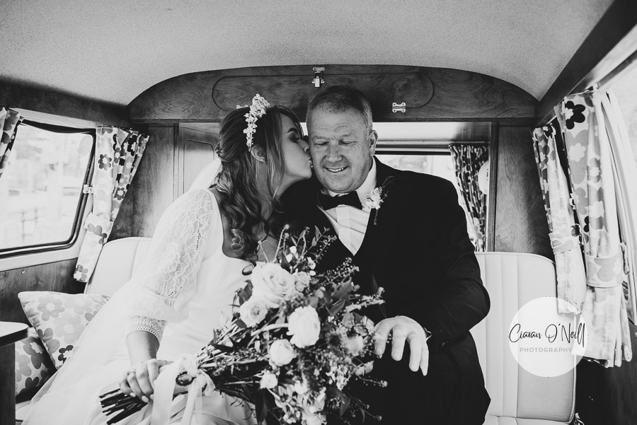 Bride kissing her father on the cheek, as they wait in the car before the wedding ceremony