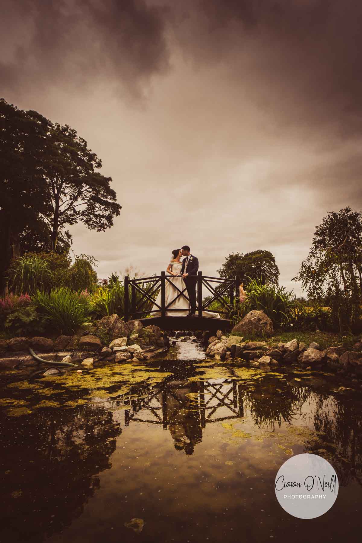 Couple kissing whilst standing on a bridge over a pond at a Darver Castle wedding