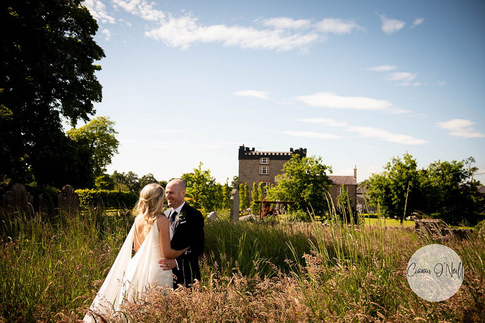Bride and groom in long grass in front of Darver Castle