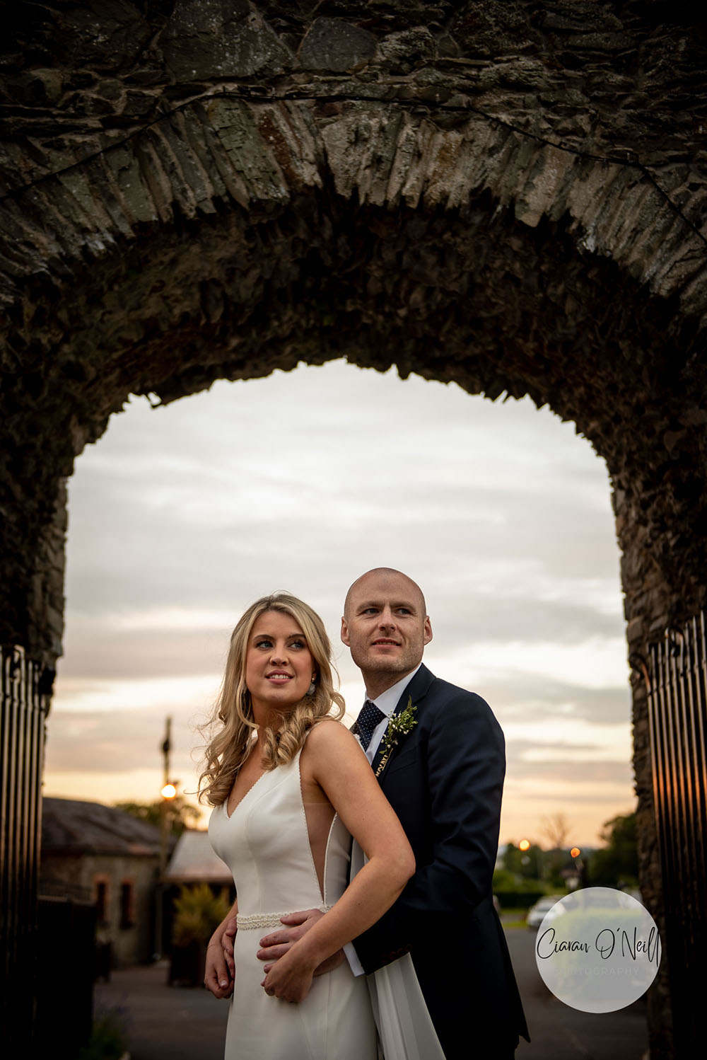 bride and groom under stone arch with sun setting