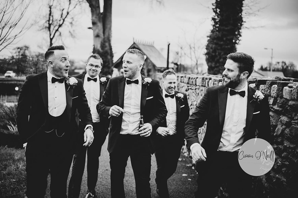 groom and men walking and laughing in black and white