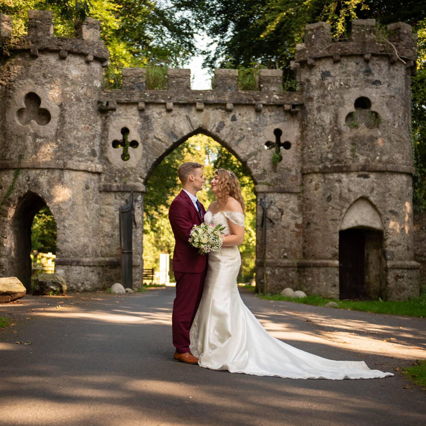 Bride & Groom embrace on the driveaway up to the beautiful archway at Tollymore Forest Park