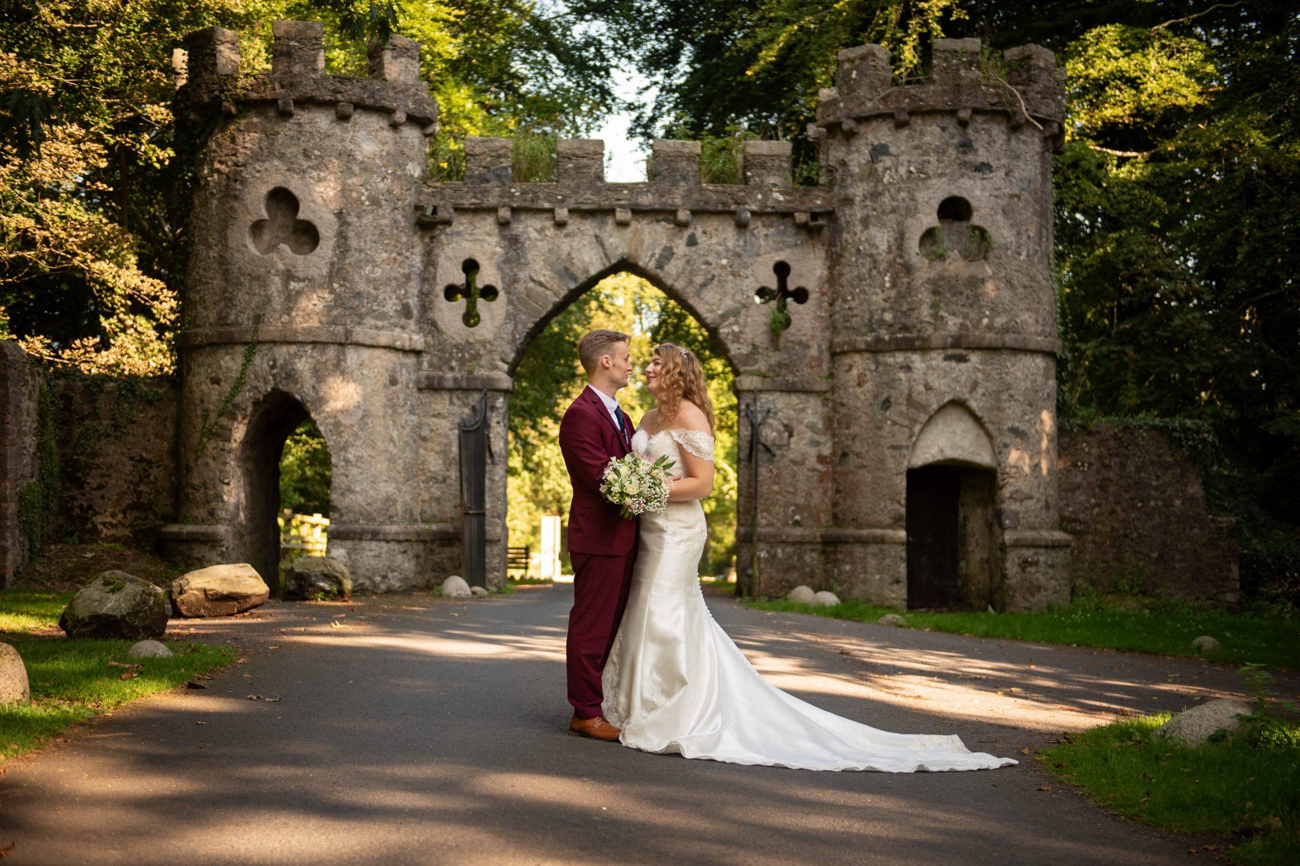 Bride & Groom embrace on the driveaway up to the beautiful archway at Tollymore Forest Park